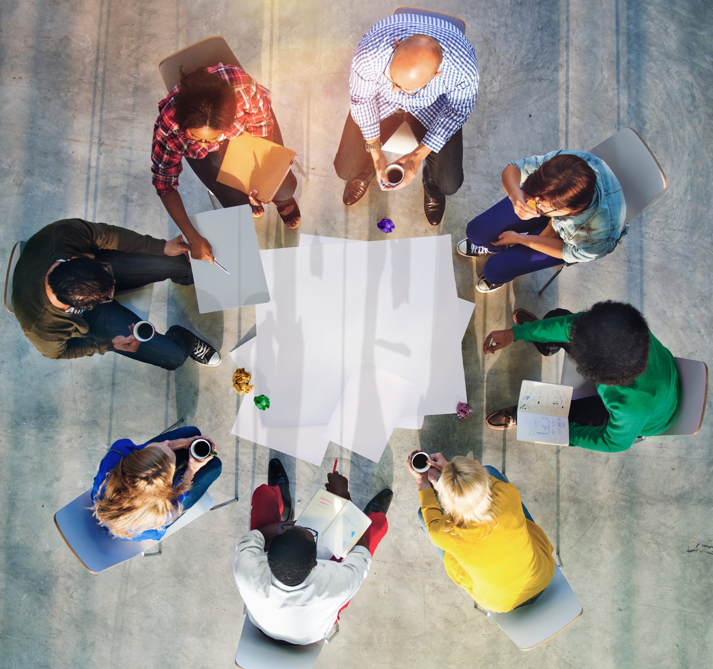 Eine Gruppe von Menschen sitzt im Kreis und diskutiert gemeinsam über Ideen, während auf dem Boden große Papierbögen liegen – Symbol für Teamarbeit und kreative Zusammenarbeit. Eine Gruppe von Menschen sitzt im Kreis und diskutiert gemeinsam über Ideen, während auf dem Boden große Papierbögen liegen – Symbol für Teamarbeit und kreative Zusammenarbeit.